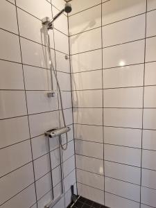 W łazience z białymi ścianami wyłożonymi kafelkami znajduje się prysznic. w obiekcie Lägenhet Yvonne w mieście Gränna