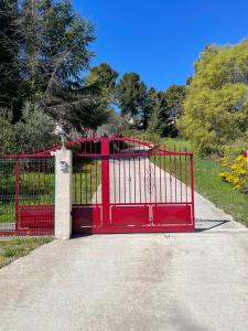 een rode metalen poort in een park met bomen bij Au Perchoir in Caunes-Minervois