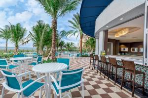 un patio con mesas, sillas y palmeras en Residence Inn Fort Lauderdale Pompano Beach/Oceanfront, en Pompano Beach