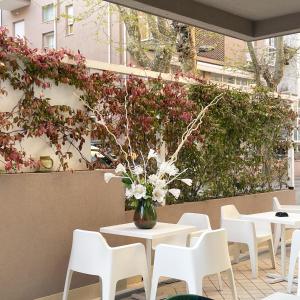 un patio con mesas, sillas y flores en un jarrón en Hotel Little en Rímini
