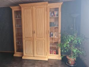 a wooden cabinet with books in it next to a plant at FeWo-Am-Nationalpark-Eifel in Nideggen
