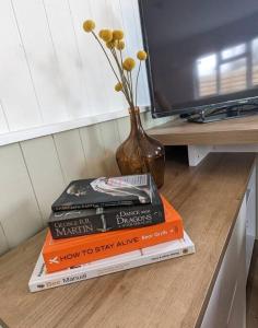 a pile of books sitting on a table with a vase at Cotts Cabin - Welcombe - 2 min walk to pub in Bideford