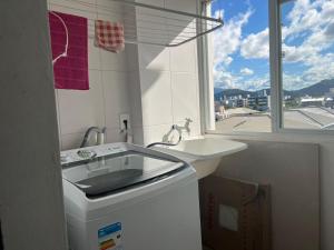 een witte badkamer met een wastafel en een raam bij Lindo apartamento completo e com garagem coberta in Palhoça