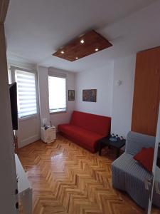 Apartman Natalija في Kuršumlija: غرفة معيشة مع أريكة حمراء على أرضية خشبية