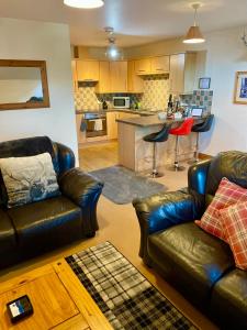 a living room with two leather couches and a kitchen at Grey Stag Apartment in Nairn