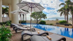 a row of lounge chairs with umbrellas next to a swimming pool at Costa Executive Residences in Nha Trang