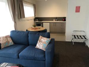 uma sala de estar com um sofá azul e uma cozinha em Coachman Motel em Christchurch