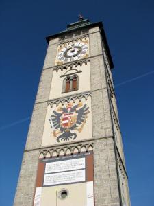 ein hoher Turm mit einer Uhr und einem Wappen darauf in der Unterkunft Turmhotel in Enns