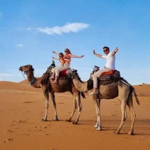 three people riding on the backs of camels in the desert at Bivouac Camel Trips in Merzouga
