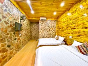 two beds in a room with a stone wall at Lan Rừng Homestay in Lũng Niêo