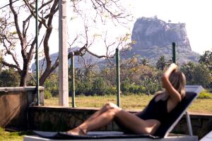 a woman sitting in a chair with a mountain in the background at Royal Rock Sigiriya in Sigiriya