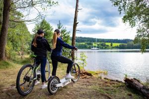 two women riding bikes next to a lake at Amenity Hotel & Resort Lipno in Lipno nad Vltavou