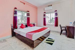 Schlafzimmer mit einem Bett mit roten Vorhängen und einem Tisch in der Unterkunft OYO Satya Homes in Khandagiri