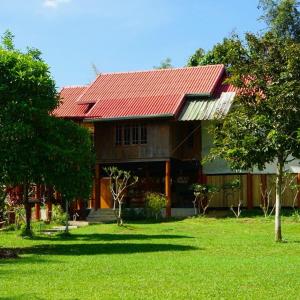 ein Haus mit rotem Dach auf einem grünen Hof in der Unterkunft BaanRai KhunYa บ้านไร่คุณย่า in Sai Yok