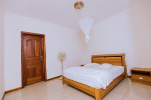 een slaapkamer met een bed met witte lakens en een deur bij KAMI LUXURY APARTMENTS in Kigali