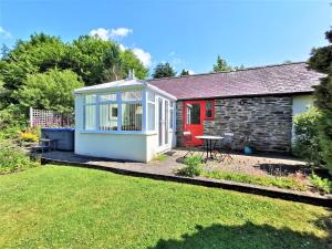 um pequeno chalé com uma porta vermelha e um quintal em Romantic Cottage with Private Hot Tub em Llanfyrnach