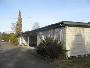 a white building with a large window next to a street at Tongariro River Motel in Turangi