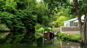 a small boat on a river with trees and a building at Thornton Manor - Holiday Cottages and Apartments in Heswall