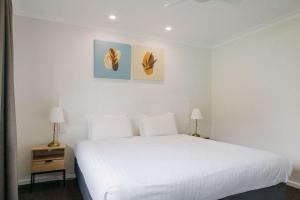 a white bedroom with a large white bed and two lamps at Quality Apartments Banksia Albany in Albany