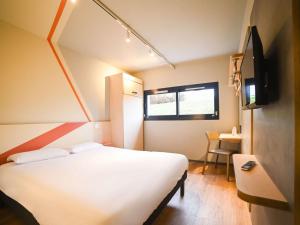 a bedroom with a white bed and a television at ibis budget Site du Futuroscope in Chasseneuil-du-Poitou