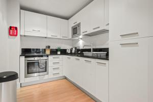 eine weiße Küche mit Küchengeräten aus Edelstahl und weißen Schränken in der Unterkunft One Bed Serviced Apartment near Blackfriars in London