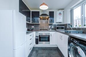 cocina con armarios blancos, lavadora y secadora en Chic 2 Bed House with Garden & Free Parking, en Mánchester