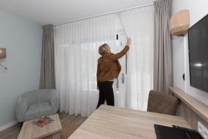 un hombre está abriendo una ventana en una habitación en Beach Hotel I Kloeg Collection, en Zoutelande