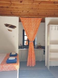 a bedroom with an orange curtain and a kitchen at Arancio independent room in Ecovilla on the beach in Apolakkiá