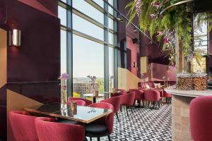 a restaurant with red chairs and tables and windows at The Den, 's-Hertogenbosch, a Tribute Portfolio Hotel in Den Bosch