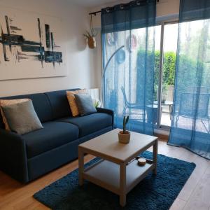 a living room with a blue couch and a table at Cosy studio le Garden ensoleillé in Cabourg
