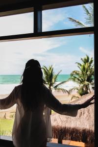 uma mulher em pé em frente a uma janela com vista para a praia em Anauí Pousada em Porto de Galinhas