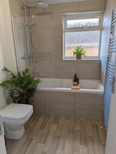 a bathroom with a tub and a toilet and a window at Cosy 4 Bedroom Town House Ample Parking & Netflix in Leominster