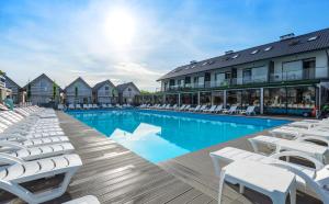 a swimming pool with white lounge chairs next to a building at Holiday Park & Resort Grzybowo in Grzybowo