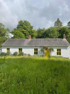 une maison blanche avec des fenêtres jaunes dans un champ dans l'établissement Newly renovated Cottage with private trout fishing set in beautiful wildlife estate, à Monaghan