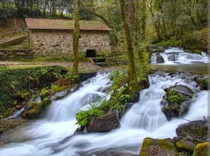 a waterfall in front of a stone building next to a river at Casa Pepe in Meaño