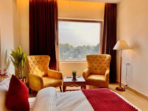 um quarto de hotel com duas cadeiras e uma cama e uma janela em Ganges blossam - A Four Star Luxury Hotel & Resort em Haridwar