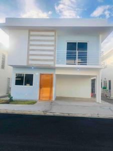 a white house with a brown door on a street at Casa en Baní cerca de la playa in Baní