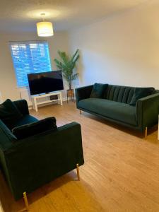 uma sala de estar com 2 sofás verdes e uma televisão de ecrã plano em Kingmaker House! Luxury 4 Beds - Free Private Parking and Garden em Northampton