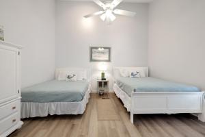 a white bedroom with two beds and a ceiling fan at Chic Townhouse Steps to the Beach Outdoor Pools in Panama City Beach