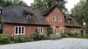 uma casa com telhado de palha e um banco à frente em Reetdachhaus Warft Simmerdeis - Maisonettewohnung em Oldenswort