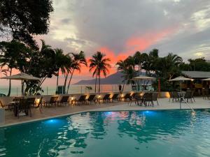 a pool with chairs and a sunset in the background at Porto Paúba Flat 116 in Pauba
