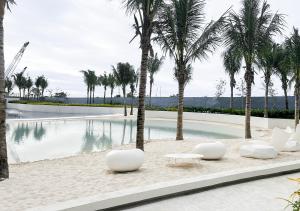 a swimming pool with palm trees and white chairs at Largest 2-Bed Studio in Azure North, Pampanga in San Fernando