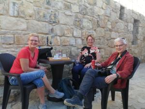 3 persone sedute su sedie di fronte a un muro di pietra di Dana Gardens Hotel a Dana