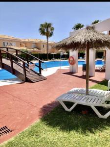 House sleeps 6, large pool walk to beach في فيرا: كرسي عشب مع مظلة من القش بجوار حمام سباحة