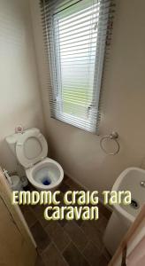 a bathroom with a toilet and a sink and a window at EMDMC Craig Tara Caravan in Ayr