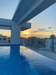 a swimming pool on the roof of a building with the sunset at Luxury 2Bedr, 2 Balcony Pool, Gym, Downtown Santo Domingo in Santo Domingo