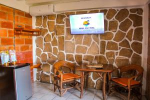 TV colgada en una pared de piedra con mesa y sillas en HANGA ROA HOTEL, en Montañita