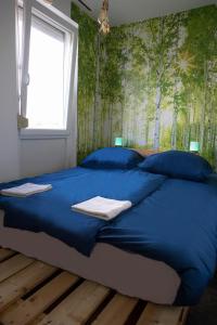 a blue bed in a bedroom with a wall with trees at Városi Apartman in Pécs