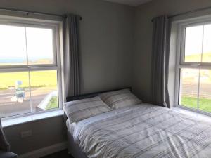 a bedroom with a bed and two windows at Dunshamrock @Sheep Island View in Ballintoy