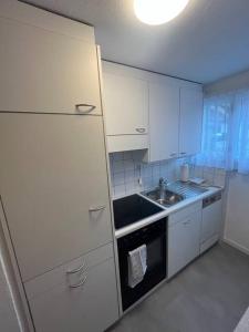 uma cozinha com armários brancos, um lavatório e um fogão em Alpina Appartment Kandersteg em Kandersteg